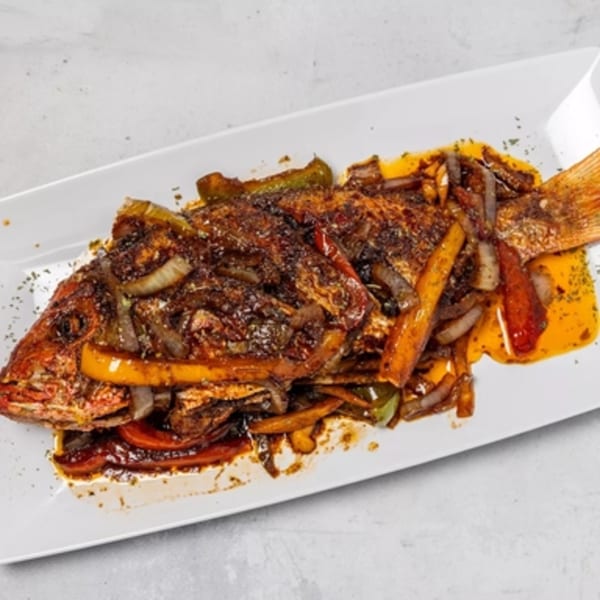 Whole fried Jamaican fish, seasoned with dark spices, onions, and bell peppers on a white platter.