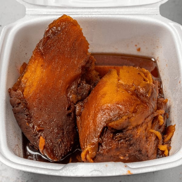 Two pieces of Jamaican stewed sweet potato pudding in a white takeout container.