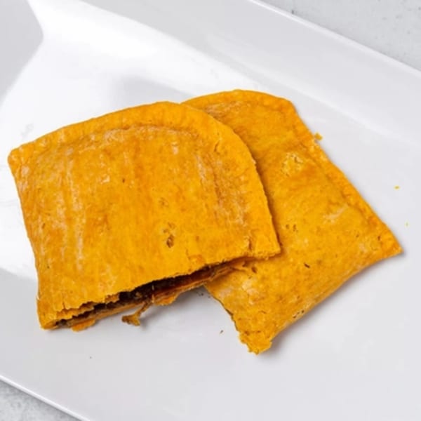 Two golden-brown Jamaican beef patties with flaky crusts, one slightly open revealing the filling, on a white plate.