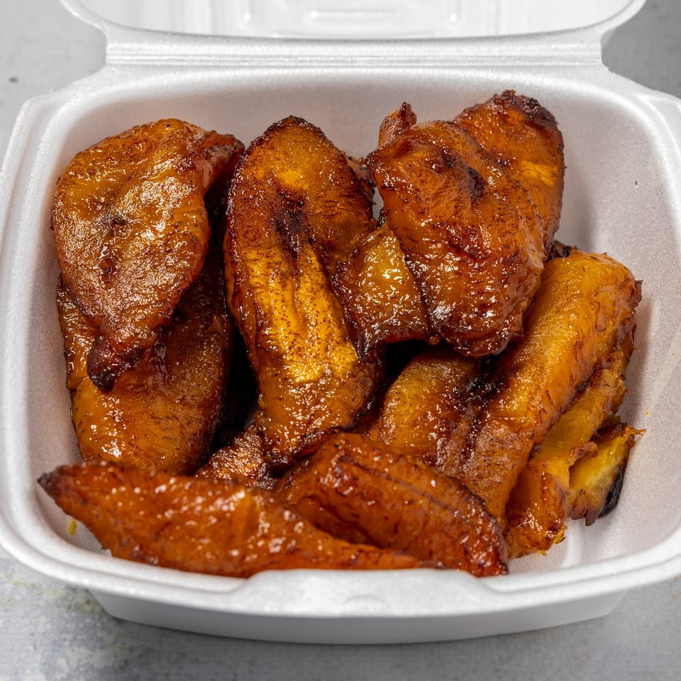 Sweet fried plantains, known as 'Irie Nation's Plantains', served in a white takeout container.