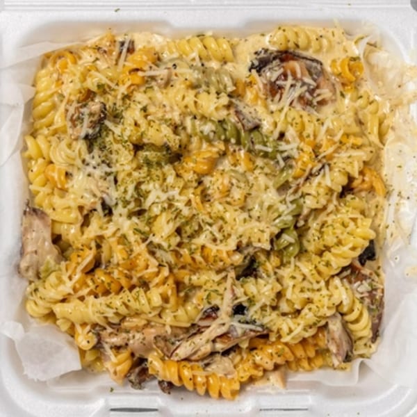 Creamy Jamaican pasta with rotini, mushrooms, and herbs in a white takeout container.