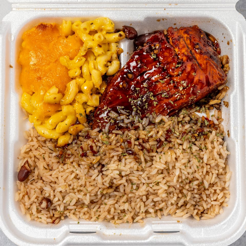Jamaican jerk chicken with rice and peas, and macaroni and cheese in a takeout container.