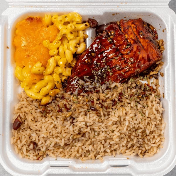 Jamaican jerk chicken with rice and peas, and macaroni and cheese in a takeout container.