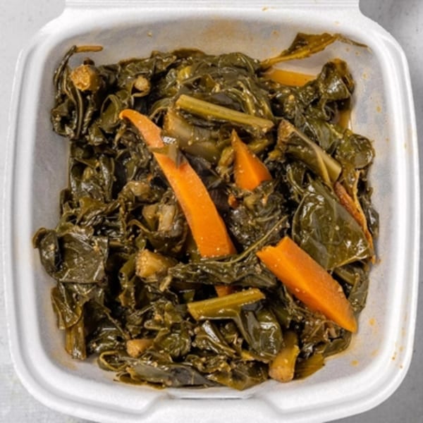 Stewed collard greens with carrots in a white takeout container from Irie Nation Restaurant.