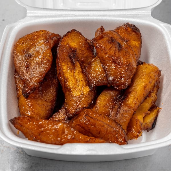 Close-up of golden-brown fried plantains in a white takeout container from Irie Nation.