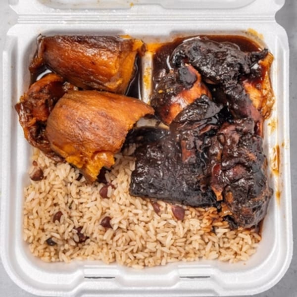 Jamaican oxtail and stew chicken with rice and peas in a white takeout container.
