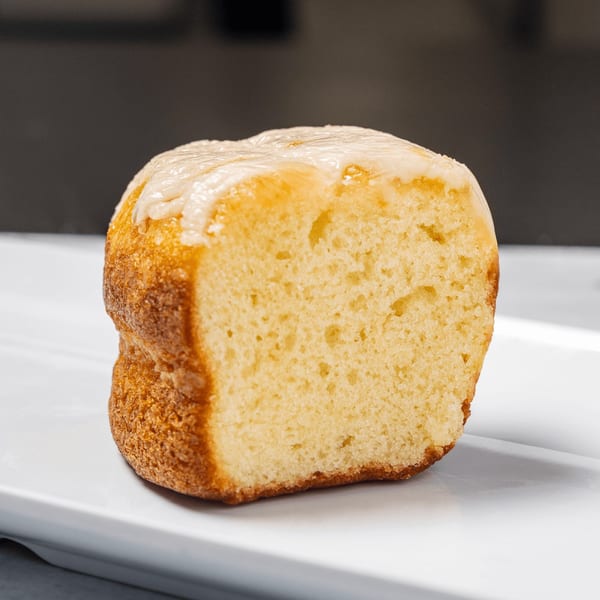 A golden-brown Jamaican rum cake with white icing on a white rectangular plate.