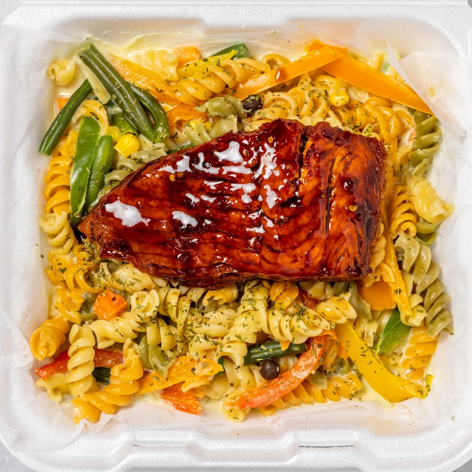 Irie Nation's Jamaican jerk salmon with colorful pasta, green beans, and bell peppers in a white takeout container.